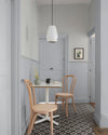 Coin repas aux murs gris perle et papier peint Maître Domino Libéron, avec table blanche, chaises en bois et suspension blanche.