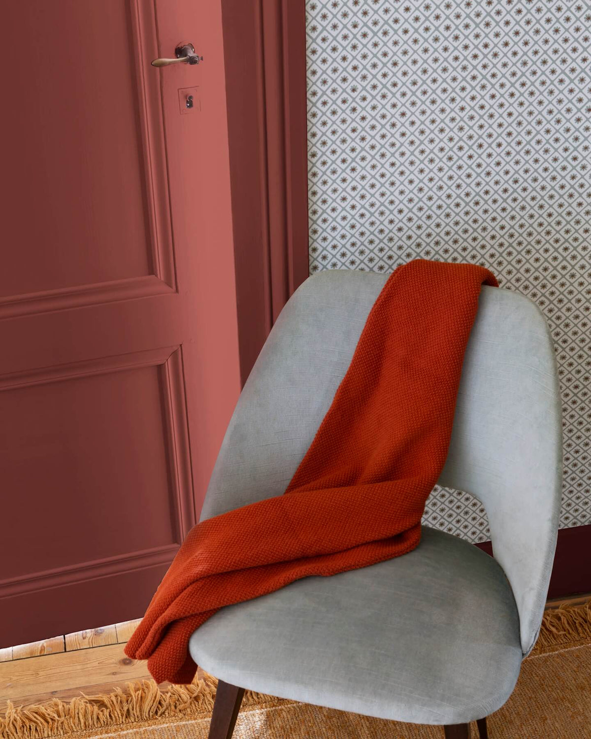 Détail d’entrée avec porte terracotta, motif géométrique Maître Domino Libéron, chaise grise et plaid rouille.