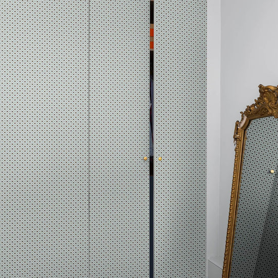 Armoire à motif géométrique Maître Domino Libéron, avec miroir doré posé au sol et parquet en bois clair.