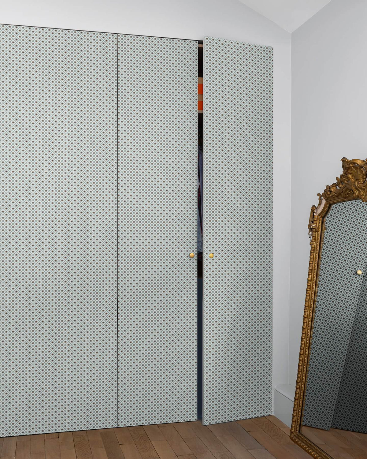 Armoire à motif géométrique Maître Domino Libéron, avec miroir doré posé au sol et parquet en bois clair.
