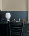 Coin bureau aux murs beige et motif géométrique bleu Maître Domino Libéron, avec chaise sombre, lampe blanche et tasse.