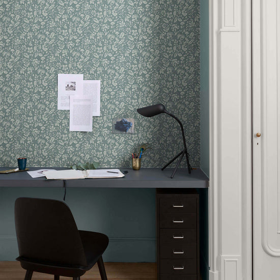 Bureau au mur floral vert d’eau et blanc, teinte Œillet Reine Libéron, avec chaise noire, lampe noire et soubassement bleu.