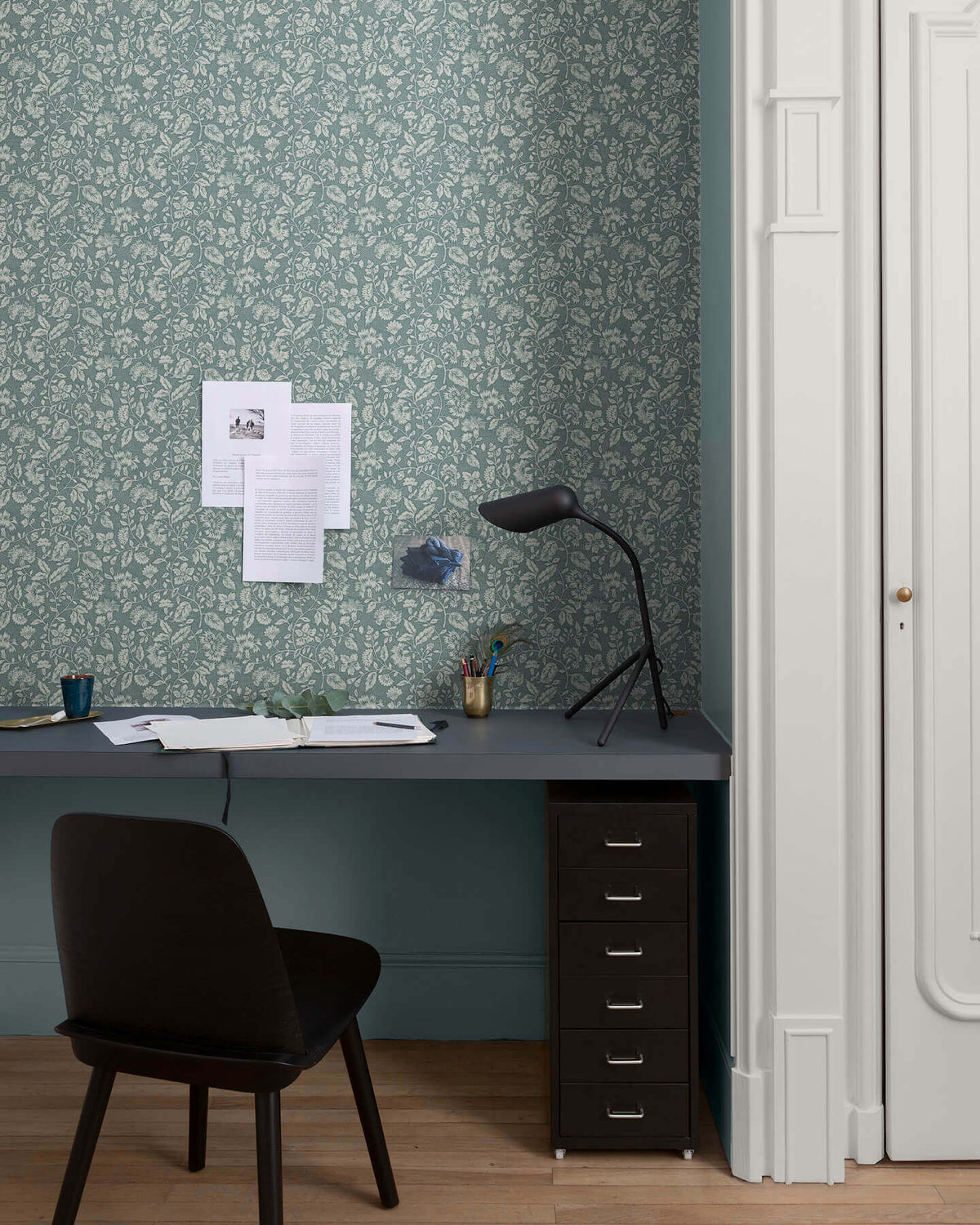Bureau au mur floral vert d’eau et blanc, teinte Œillet Reine Libéron, avec chaise noire, lampe noire et soubassement bleu.