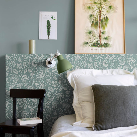 Détail de chambre aux murs vert d’eau et tête de lit florale, teinte Œillet Reine Libéron, avec lit blanc, chaise noire et lampe verte.