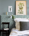Détail de chambre aux murs vert d’eau et tête de lit florale, teinte Œillet Reine Libéron, avec lit blanc, chaise noire et lampe verte.