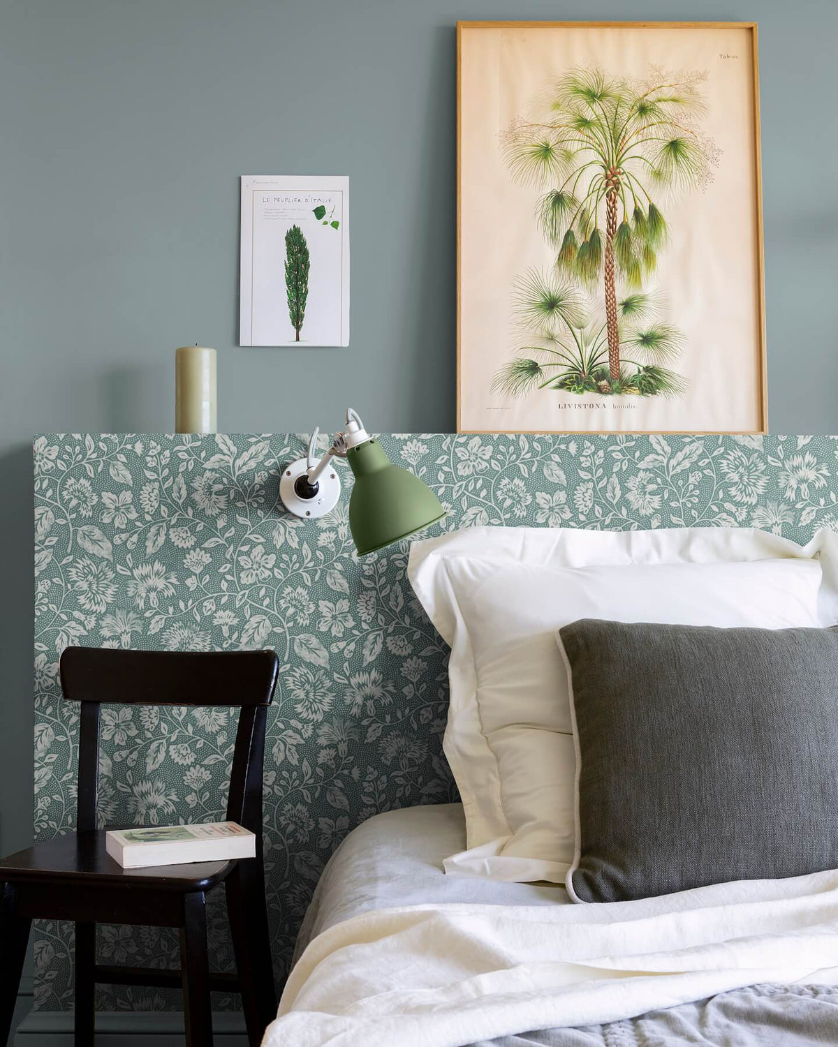 Détail de chambre aux murs vert d’eau et tête de lit florale, teinte Œillet Reine Libéron, avec lit blanc, chaise noire et lampe verte.
