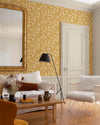 Salon au mur floral ocre et blanc, teinte Œillet Reine Libéron, avec miroir doré, canapé clair et fauteuil tressé.