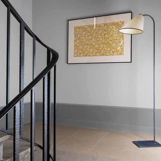 Palier à l’escalier aux murs gris avec soubassement plus foncé, cadre floral Œillet Reine Libéron et lampadaire.