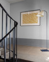 Palier à l’escalier aux murs gris avec soubassement plus foncé, cadre floral Œillet Reine Libéron et lampadaire.