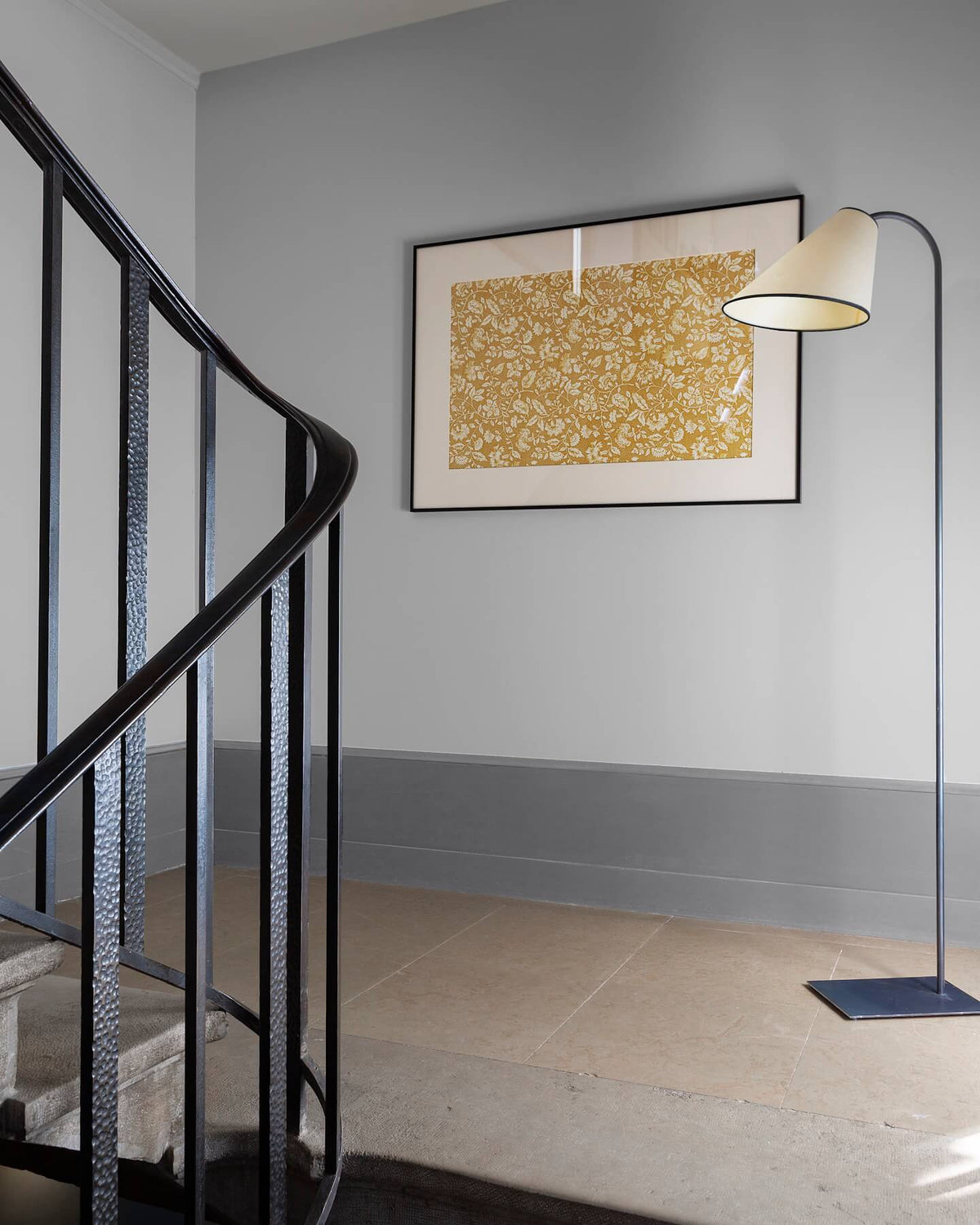 Palier à l’escalier aux murs gris avec soubassement plus foncé, cadre floral Œillet Reine Libéron et lampadaire.