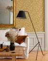 Détail de salon au mur floral ocre et blanc, teinte Œillet Reine Libéron, avec miroir doré, canapé clair et lampe noire.