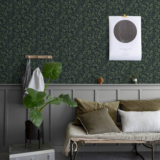 Salon au mur floral sombre, teinte Œillet Reine Libéron, avec banquette kaki, plante verte et soubassement gris.