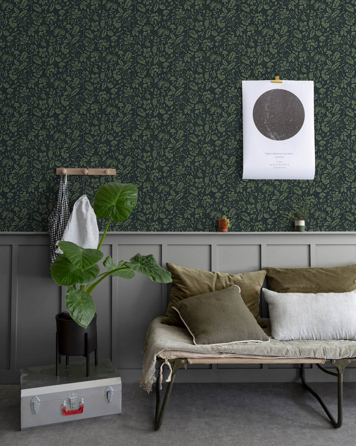 Salon au mur floral sombre, teinte Œillet Reine Libéron, avec banquette kaki, plante verte et soubassement gris.