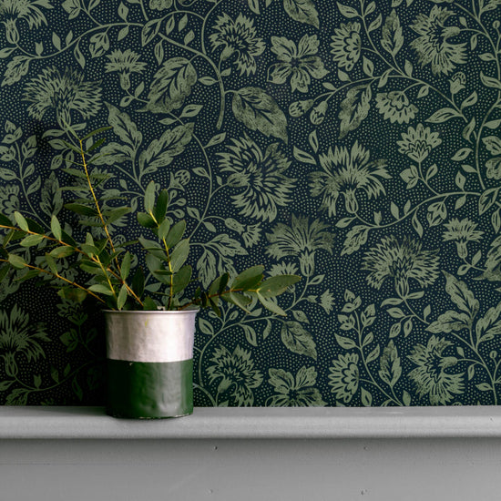 Détail de mur floral sombre, teinte Œillet Reine Libéron, avec pot de feuillage vert sur soubassement gris.