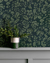 Détail de mur floral sombre, teinte Œillet Reine Libéron, avec pot de feuillage vert sur soubassement gris.