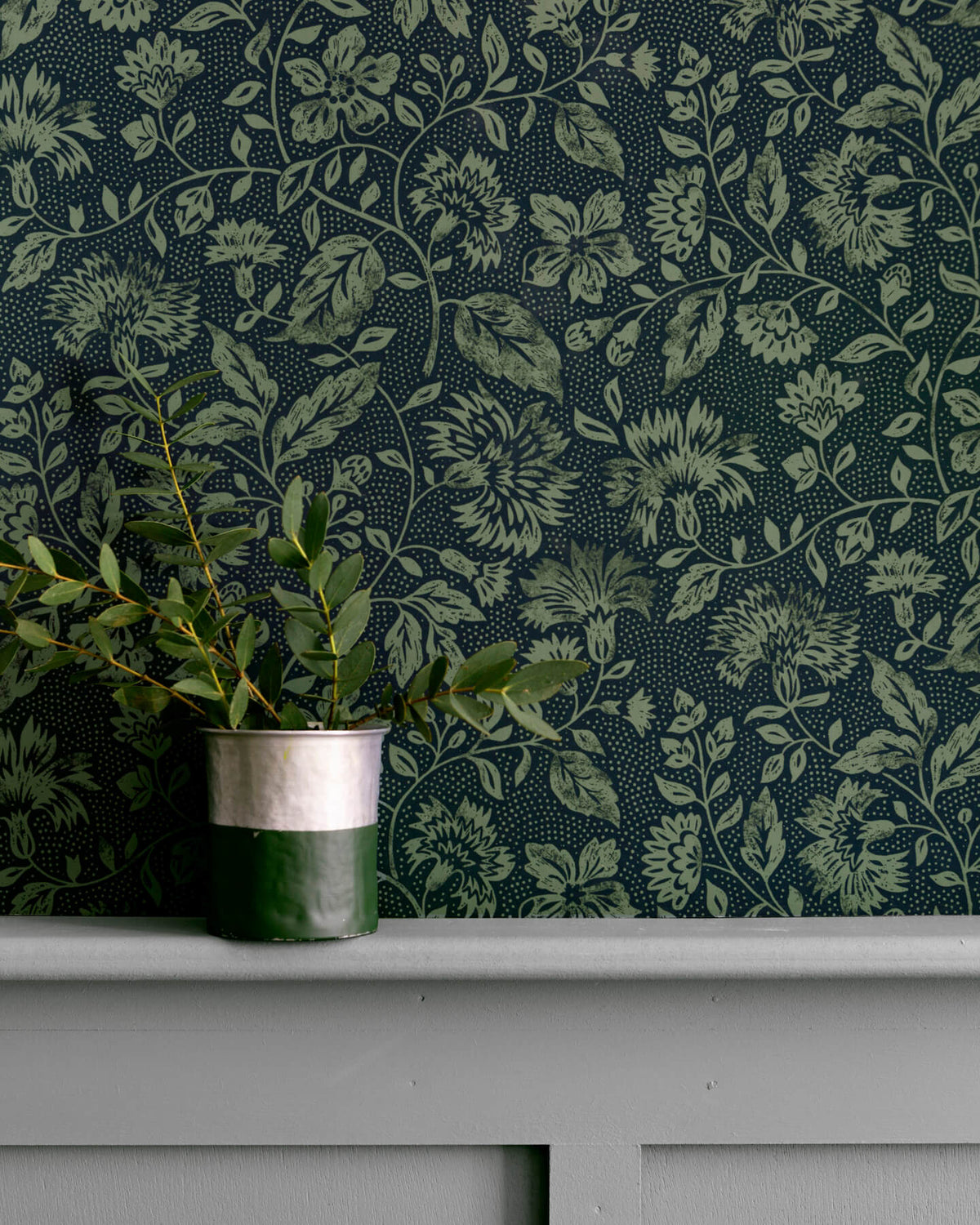 Détail de mur floral sombre, teinte Œillet Reine Libéron, avec pot de feuillage vert sur soubassement gris.