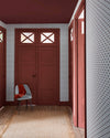 Entrée aux murs terracotta et papier peint Maître Domino Libéron, avec portes assorties, chaise grise et tapis beige.
