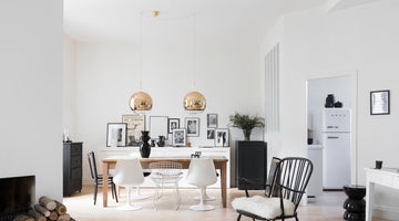 Salle à manger lumineuse aux murs blancs avant peinture Libéron, avec table en bois, chaises design et suspensions dorées.