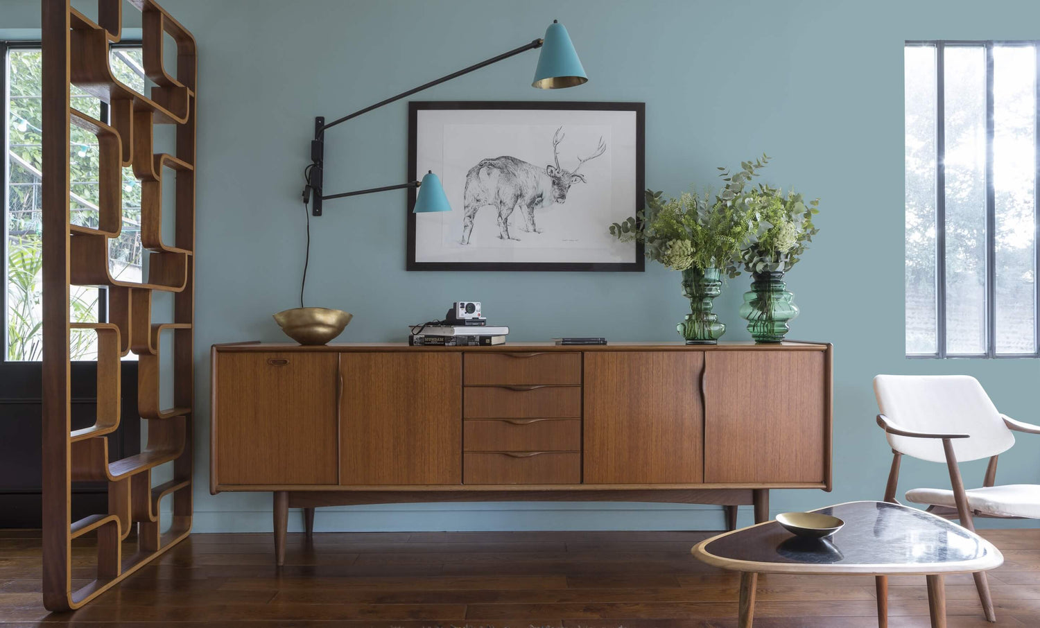 Buffet en bois ciré avec la Cire Black Bison Merisier Clair Libéron, dans un salon lumineux aux murs Fleur de Lin Velours de Peinture, avec vases verts, appliques bleues et déco vintage Libéron.