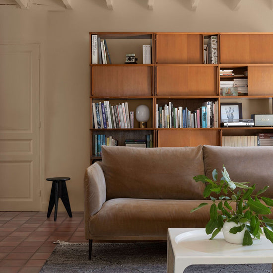 Salon avec un canapé en velours marron, une grande bibliothèque en bois et des murs peints avec la peinture Libéron Velours de Peinture, teinte Beige Paris-Brest.   