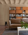 Salon avec un canapé en velours marron, une grande bibliothèque en bois et des murs peints avec la peinture Libéron Velours de Peinture, teinte Beige Paris-Brest.   