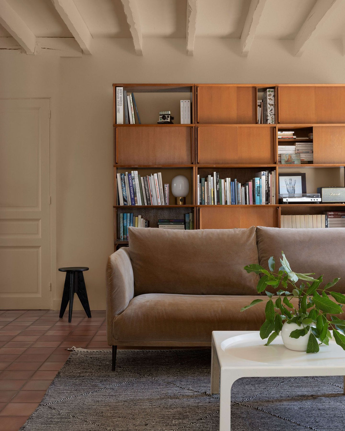 Salon avec un canapé en velours marron, une grande bibliothèque en bois et des murs peints avec la peinture Libéron Velours de Peinture, teinte Beige Paris-Brest.   
