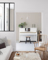 Salon aux murs blanc chiffon Libéron, avec verrière noire, piano blanc, canapé clair et chaise en bois.