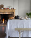 Salle à manger aux murs blanc grisaille, Velours de Peinture Libéron, avec cheminée en bois, table nappée et feu allumé.
