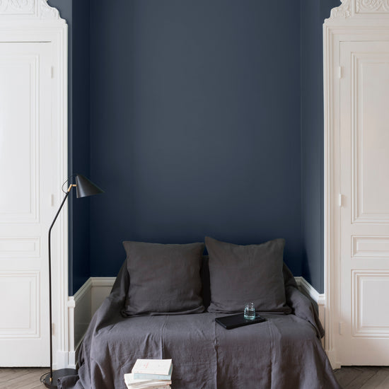 Salon aux murs bleu de chauffe, Velours de Peinture Libéron, avec canapé gris, portes blanches et parquet clair.