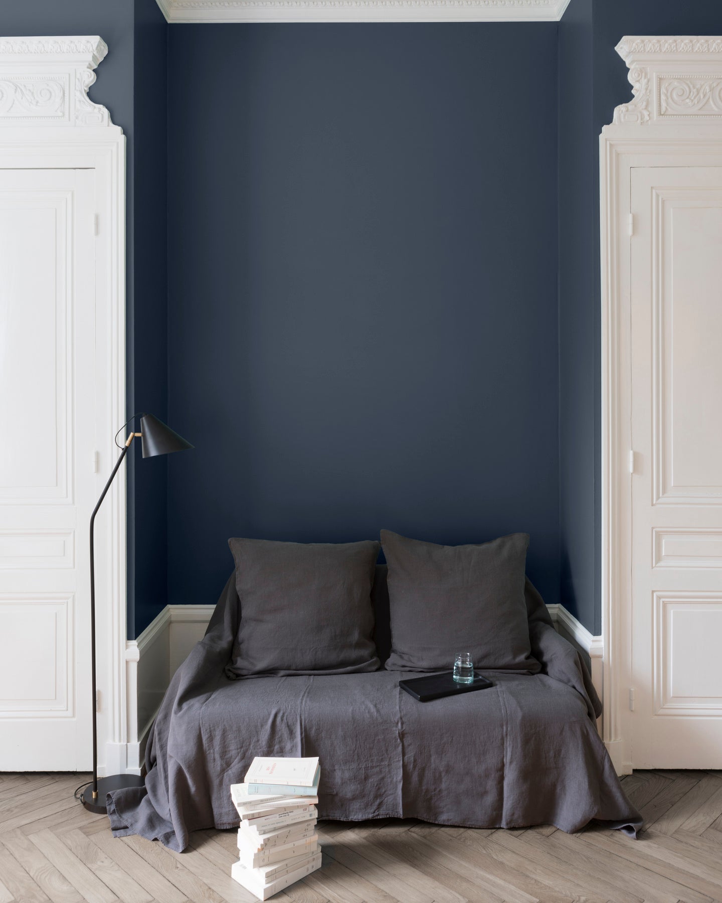 Salon aux murs bleu de chauffe, Velours de Peinture Libéron, avec canapé gris, portes blanches et parquet clair.