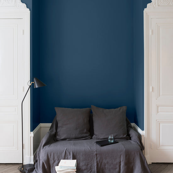 Salon aux murs bleu de minuit, Velours de Peinture Libéron, avec canapé gris, portes blanches et parquet clair.