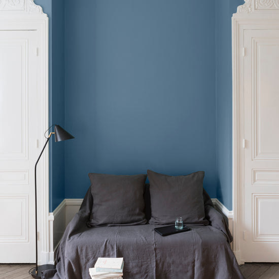 Salon aux murs Bleu de Nîmes Libéron, avec canapé gris, portes blanches, lampadaire noir et parquet clair.