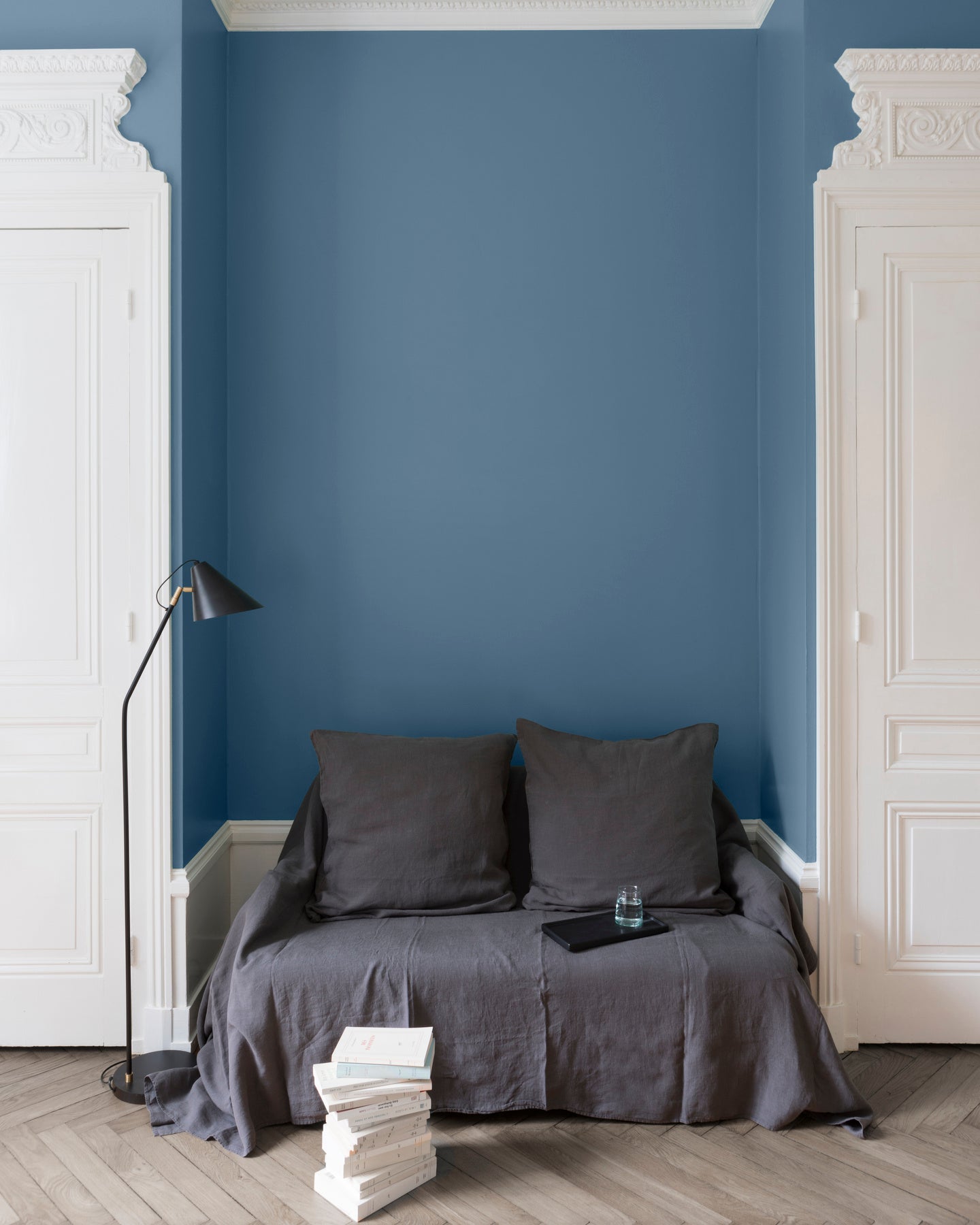 Salon aux murs Bleu de Nîmes Libéron, avec canapé gris, portes blanches, lampadaire noir et parquet clair.