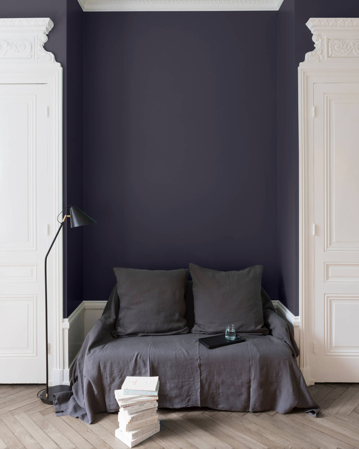 Salon aux murs bleu de Sèvres Libéron, avec canapé gris, portes blanches, lampadaire noir et parquet clair.