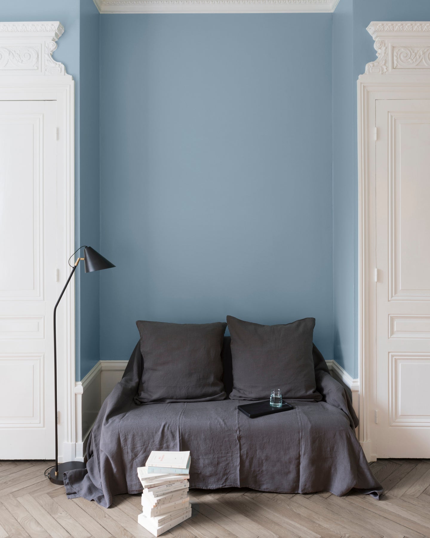 Salon aux murs Bleu Horizon Libéron, avec canapé gris, portes blanches, lampadaire noir et parquet clair.