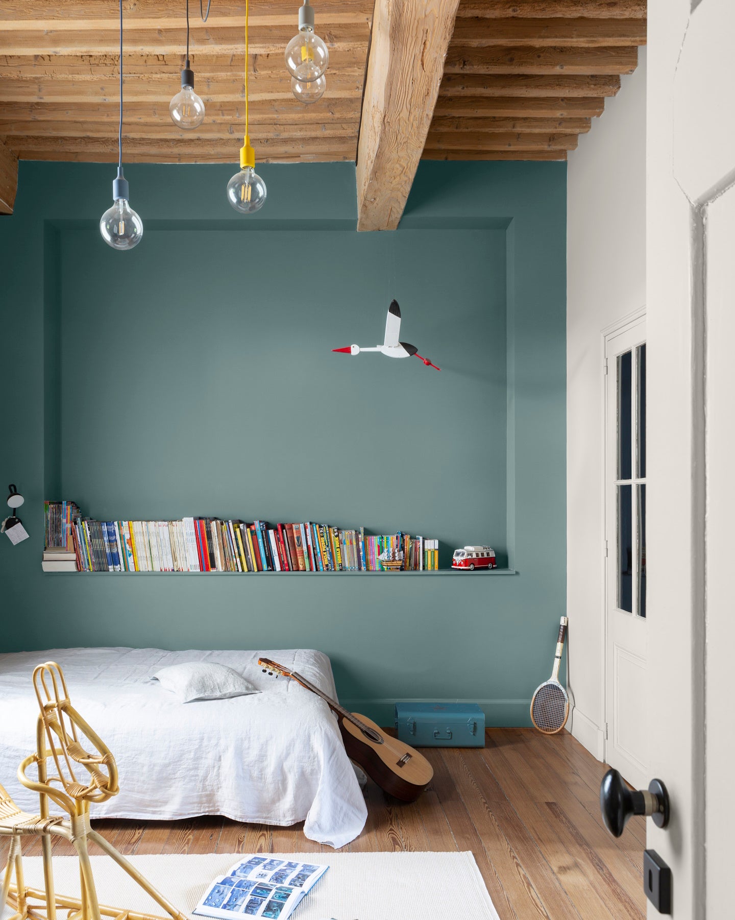 Chambre d'enfant aux murs bleus, peinture Velours de Peinture Bleu Neptune Libéron, avec poutres en bois au plafond et étagères de livres.