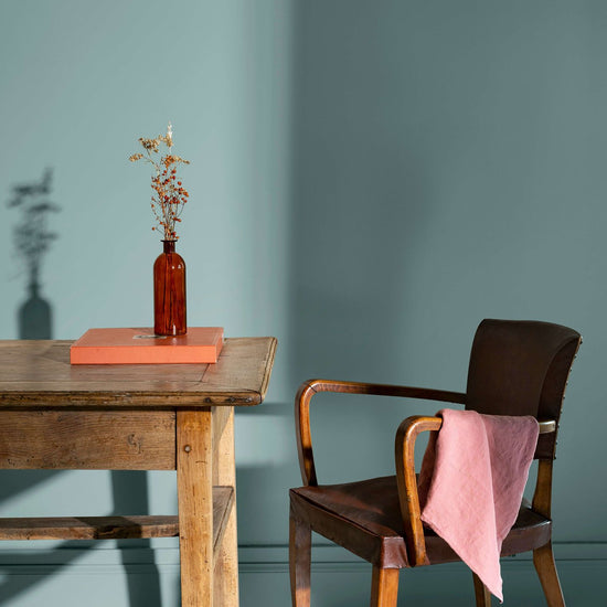 Coin de bureau avec une table rustique en bois, une chaise en cuir et des murs peints avec la peinture Libéron Velours de Peinture, teinte Bleu Neptune