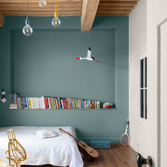 Chambre d'enfant aux murs bleus, peinture Velours de Peinture Bleu Neptune Libéron, avec poutres en bois au plafond et étagères de livres.