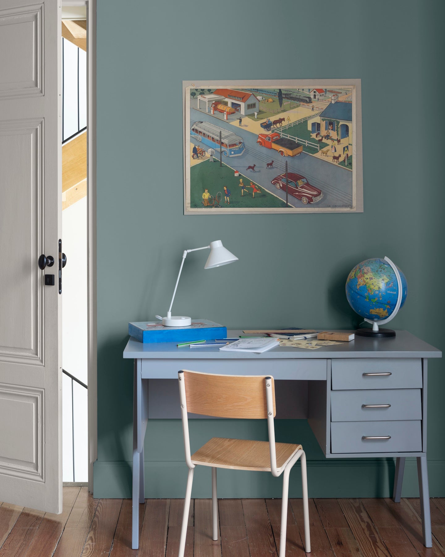 Chambre aux murs bleu Neptune, Velours de Peinture Libéron, avec bureau bleu, chaise en bois, globe et affiche vintage.