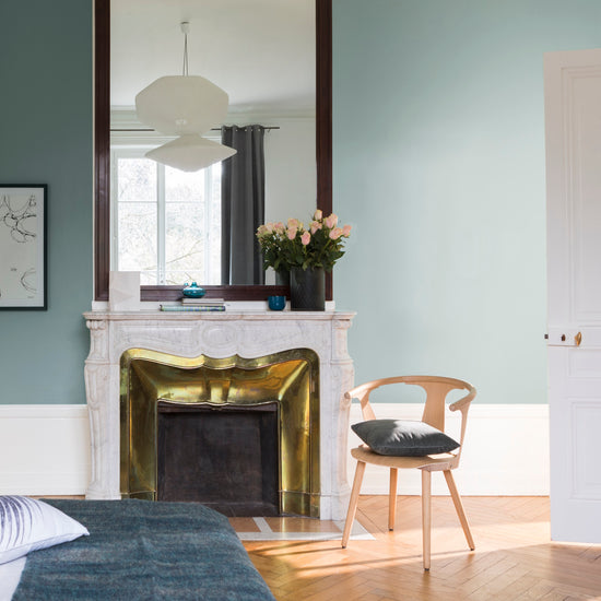 Chambre aux murs bleu Neptune, Velours de Peinture Libéron, avec cheminée en marbre, miroir et chaise en bois.