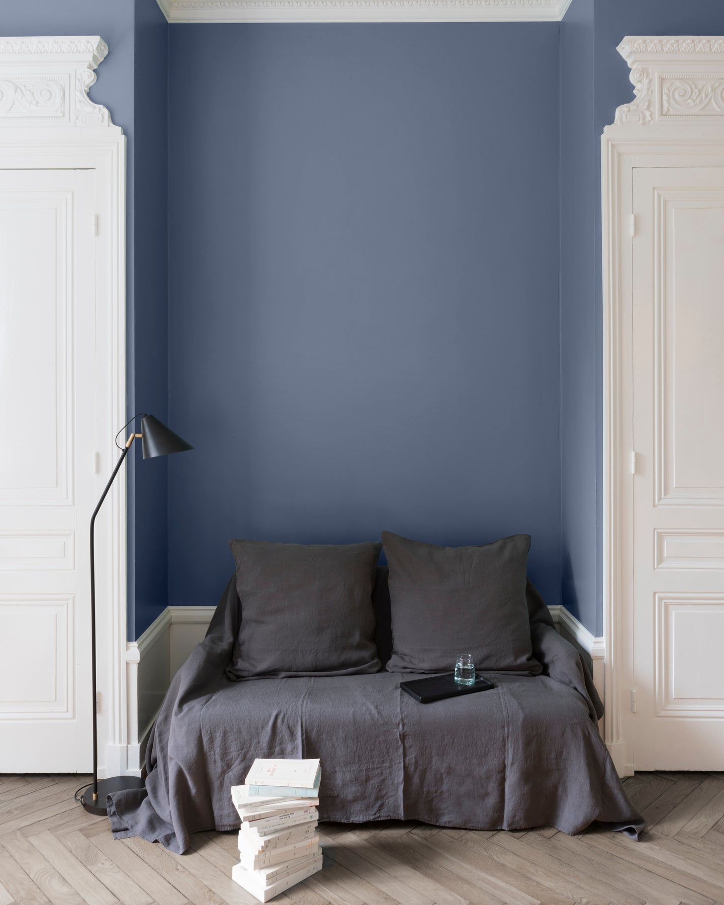 Salon aux murs Bleu Panicaut Libéron, avec canapé gris, portes blanches, lampadaire noir et parquet clair.