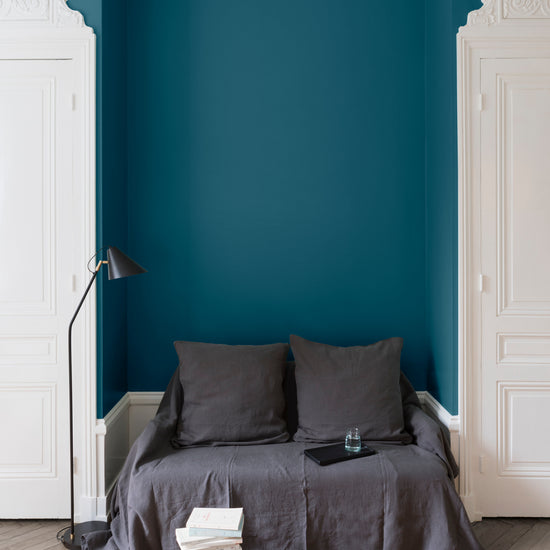 Salon aux murs bleu paon Libéron, avec canapé gris, portes blanches, lampadaire noir et parquet clair.
