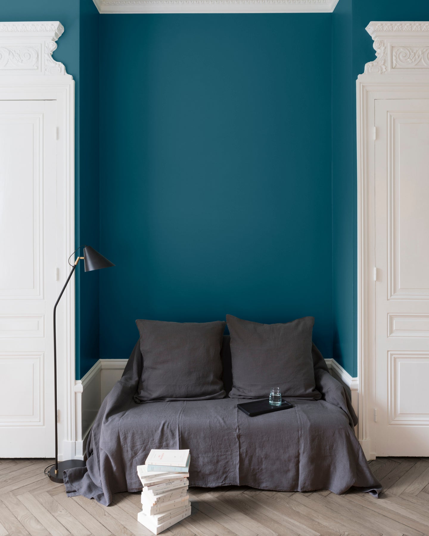 Salon aux murs bleu paon Libéron, avec canapé gris, portes blanches, lampadaire noir et parquet clair.