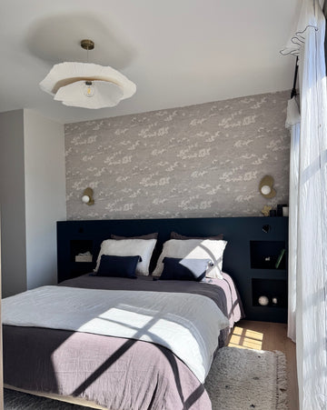 Chambre ensoleillée avec tête de nuit peinte avec 163 Faubourg Bleu de Sèvres Libéron, murs gris, draps gris et bleus, lustre et rideaux blancs