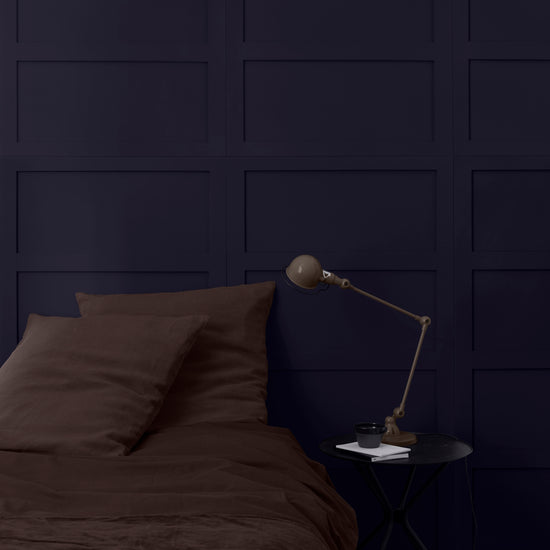 Tête de lit bleu Sèvres Libéron avec linge brun, table noire et lampe articulée dans une chambre feutrée.