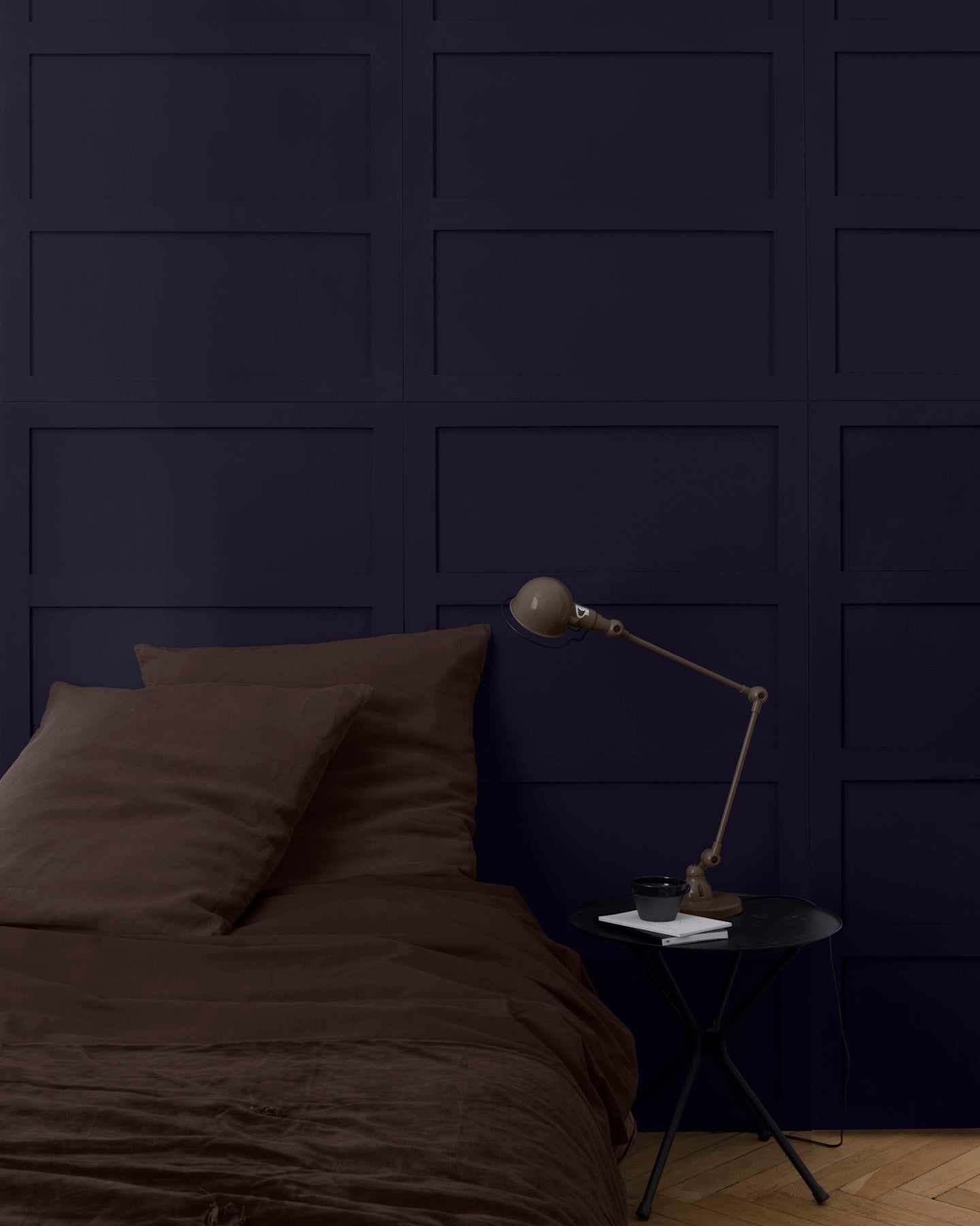Tête de lit bleu Sèvres Libéron avec linge brun, table noire et lampe articulée dans une chambre feutrée.