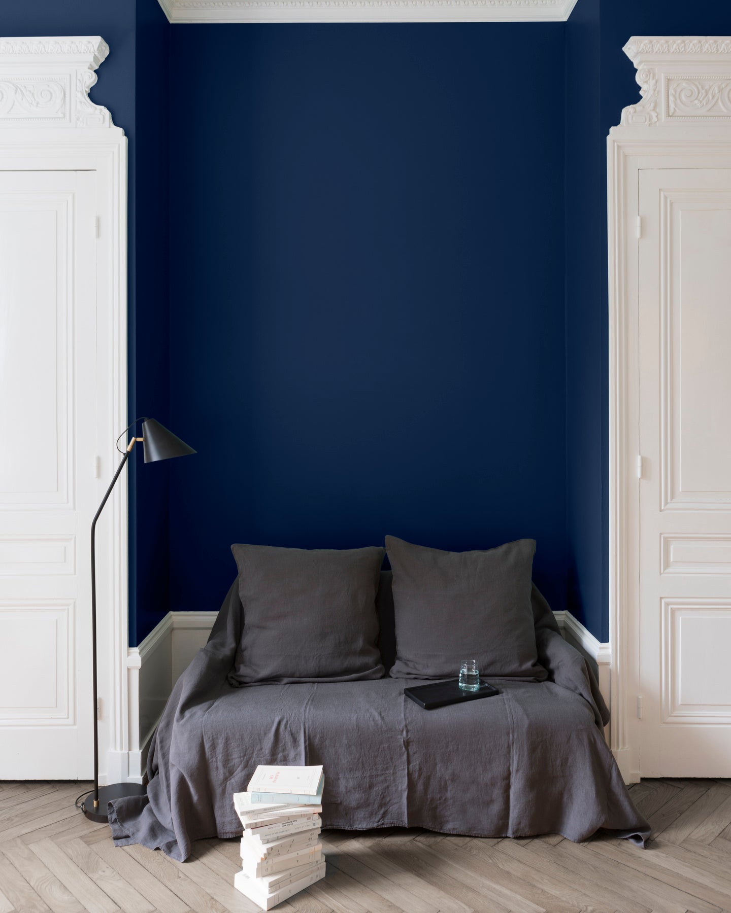 Salon aux murs Bleu Vintimille Libéron, avec canapé gris, portes blanches, lampadaire noir et parquet clair.