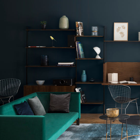 Salon aux murs bleu Vosges Libéron, avec canapé vert, bibliothèque en bois sombre et tables basses noires.