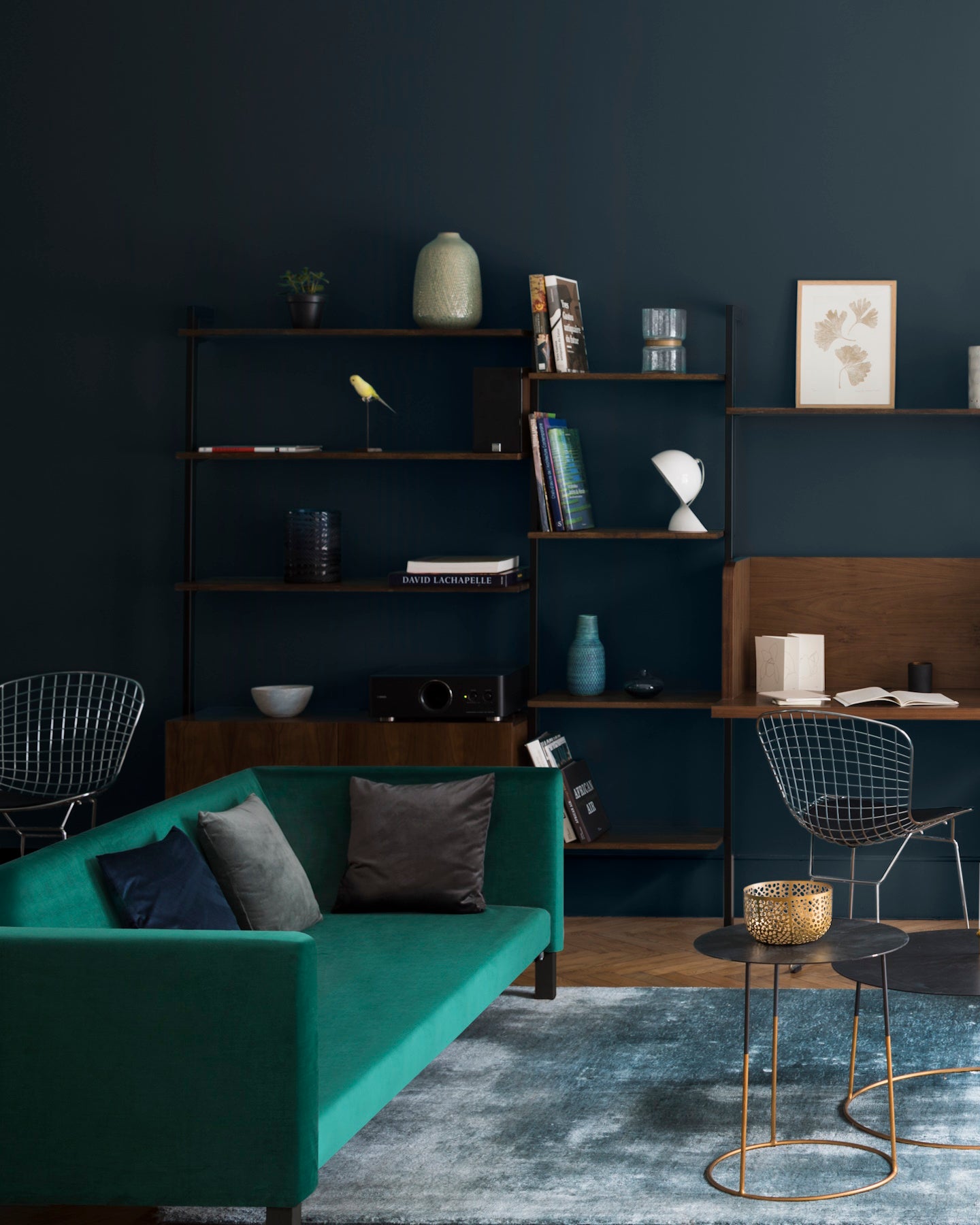 Salon aux murs bleu Vosges Libéron, avec canapé vert, bibliothèque en bois sombre et tables basses noires.