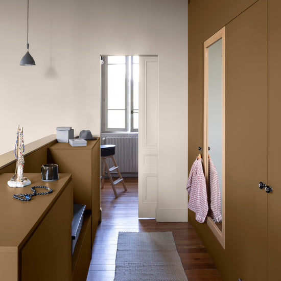 Couloir aux murs bronze astrolabe, Velours de Peinture Libéron, avec bois clair, miroir mural et tapis beige.